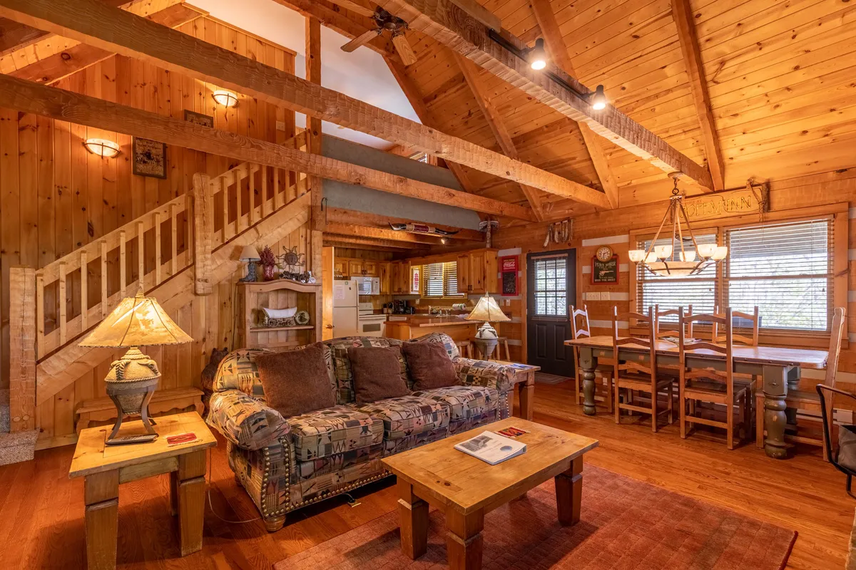This image showcases a welcoming common area featuring a sofa, a dining table, a staircase, and warm lighting from table lamps. The space feels open and inviting, ideal for family gatherings, meals, and group activities.