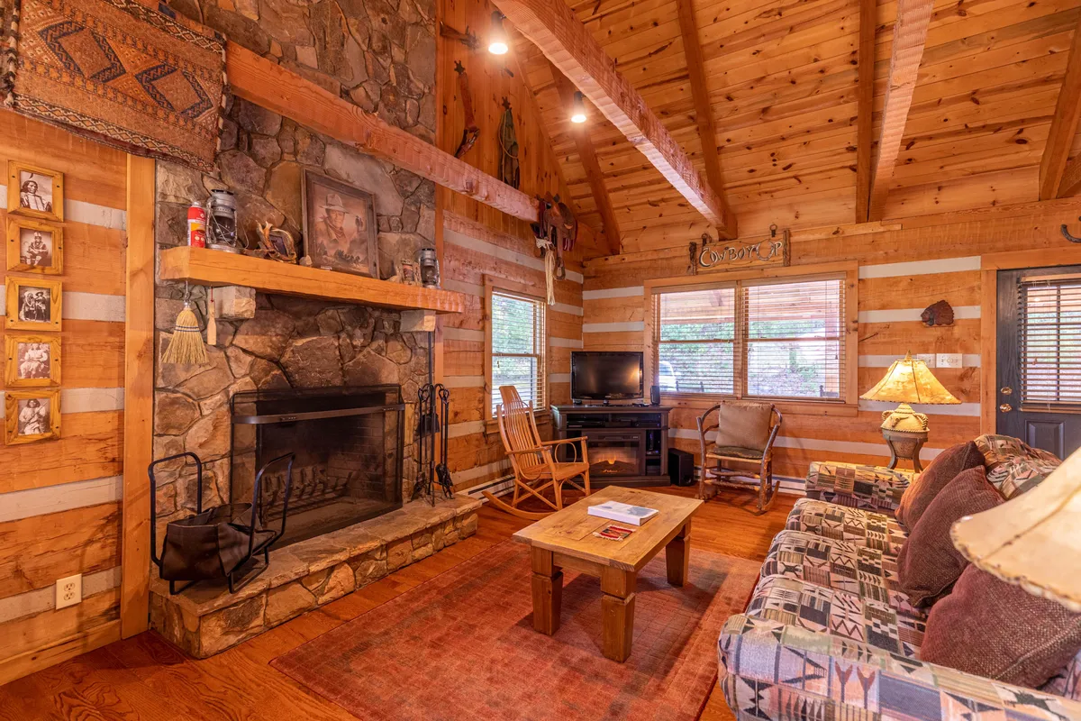 A warm, inviting living space featuring a stone fireplace as the central focal point, surrounded by comfortable seating and rustic wooden beams. Decorative artifacts add character, and the room offers plenty of space for small group gatherings, games, and relaxation after a day of adventure.