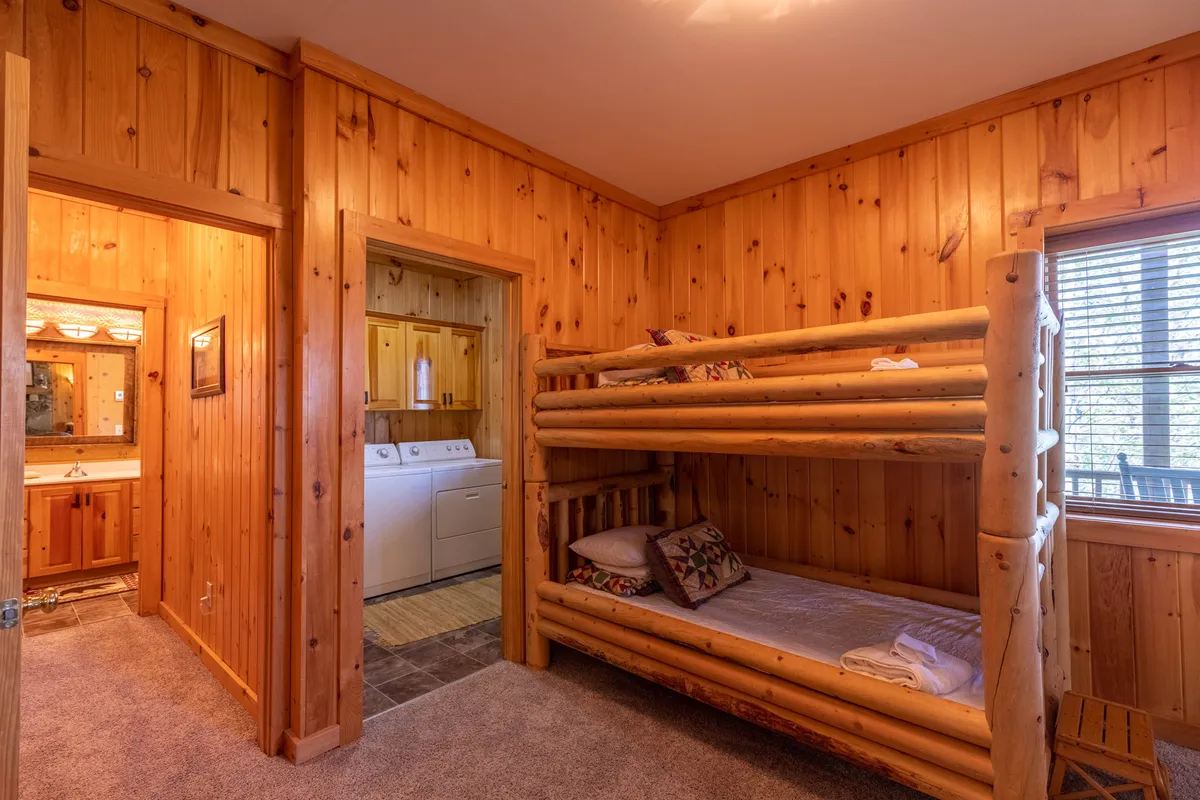 A playful basement bunk area featuring wood paneling, a cozy bunk bed, and a window with blinds. The relaxed, familial mood is ideal for children's sleepovers or a fun family retreat, echoing the section’s description of midnight giggles and shared memories.