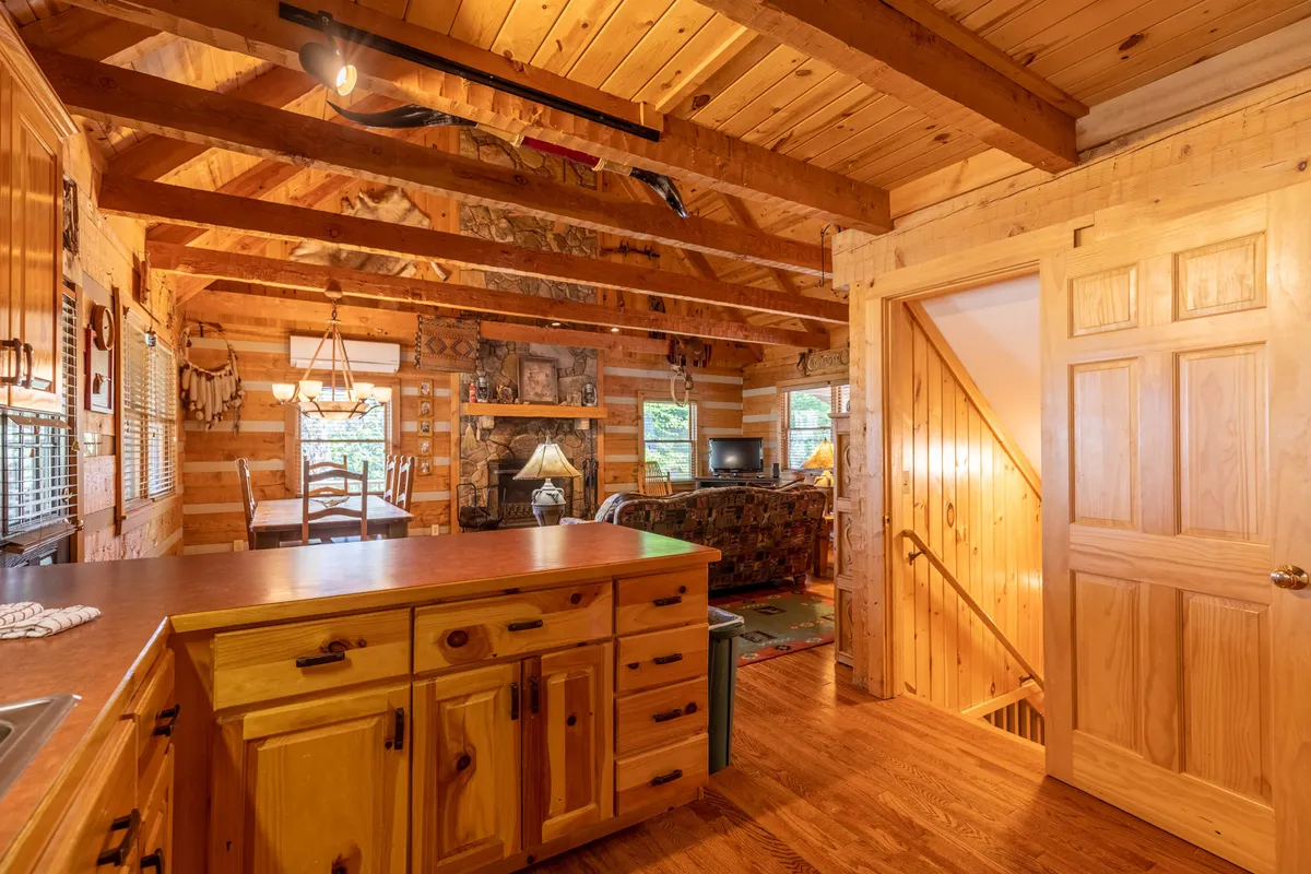A spacious open-concept area combining a kitchen with a central island, a comfortable seating area by a fireplace, and a dining table under exposed wooden beams. The flow between the kitchen, dining, and living space is evident, highlighting the opportunities for communal cooking, dining, and relaxing together.