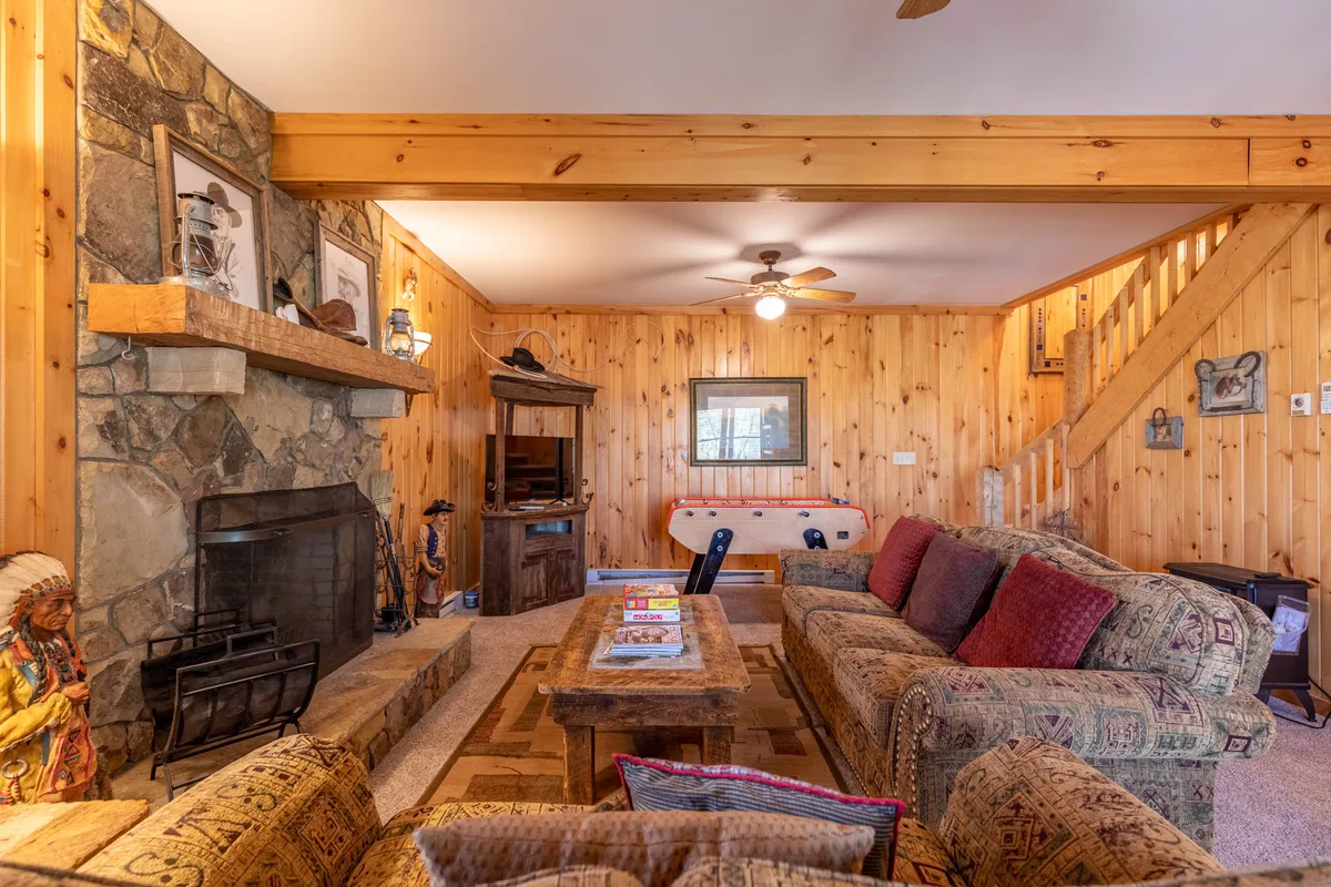 A cozy living area with a stone fireplace, wooden staircase, comfortable sofas, and a coffee table. The space is well-suited for casual conversation, game nights, and memorable family gatherings.