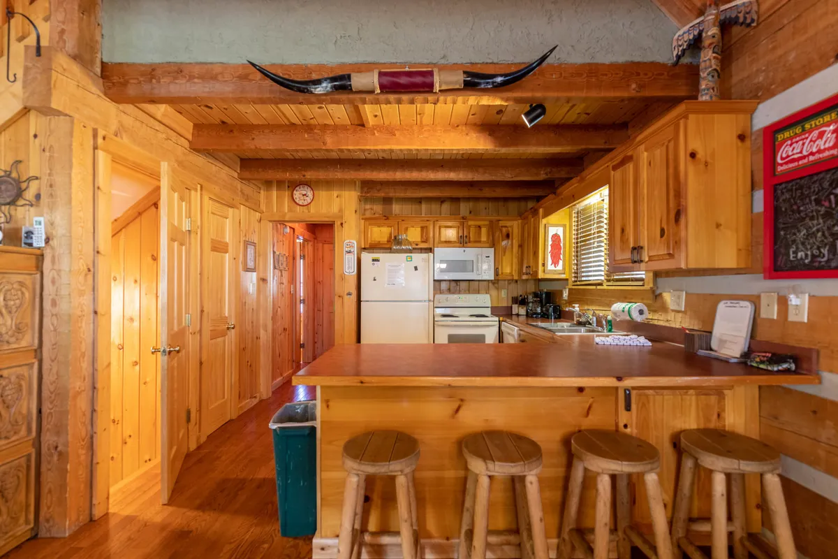 A warm and inviting kitchen scene with rustic wood bar stools at a long kitchen counter, wooden cabinets, and unique mountain-themed décor. The setup invites group meals, socializing, and creative cooking sessions, reinforcing the idea of home-cooked feasts and friendly gatherings.