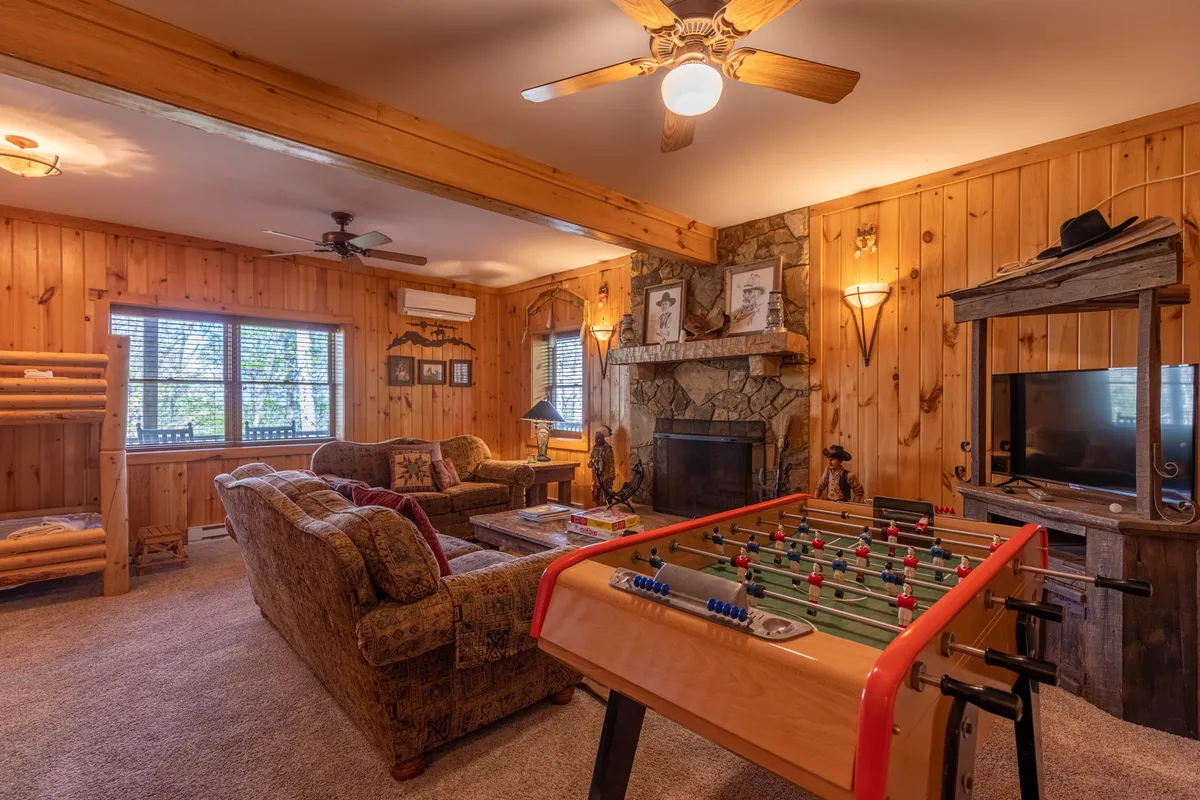 A cozy game room featuring a foosball table set before a stone fireplace, with rustic wooden furniture providing a comfortable setting. The atmosphere is friendly and relaxed, perfect for lively games and socializing.