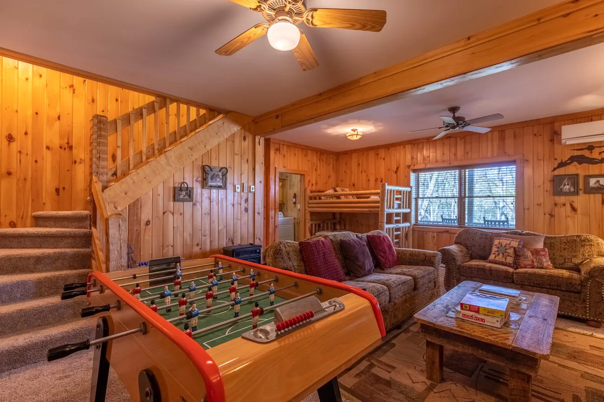 A vibrant multi-use space with a foosball table, comfortable sofas, a wooden staircase, and a set of bunk beds tucked nearby. The room feels playful and relaxed, inviting group activities and shared family moments.