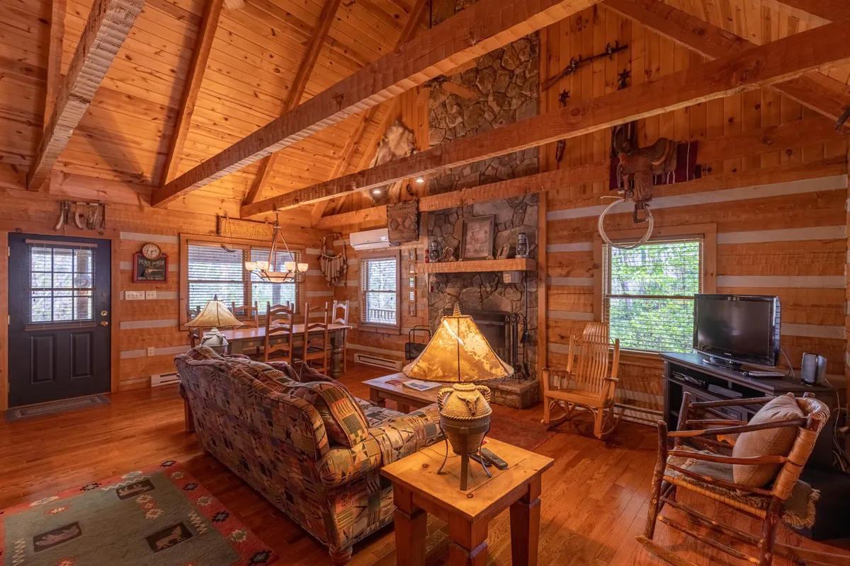 A spacious living area with a stone fireplace, exposed wooden beams, a comfortable sofa, and a dining table. The room’s warm lighting invites cozy gatherings, movie nights, and group activities, capturing the essence of leisure and connection.