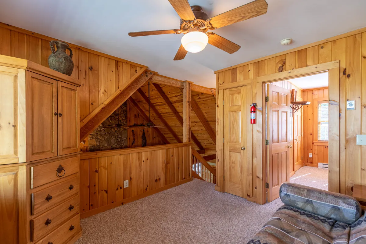 A spacious, open area with sturdy wooden furniture, a ceiling fan, and a wooden staircase, illuminated by sunlight streaming in through multiple windows. The room's practicality and durability are complemented by textured wall panels, making it a welcoming space suitable for families and their pets.