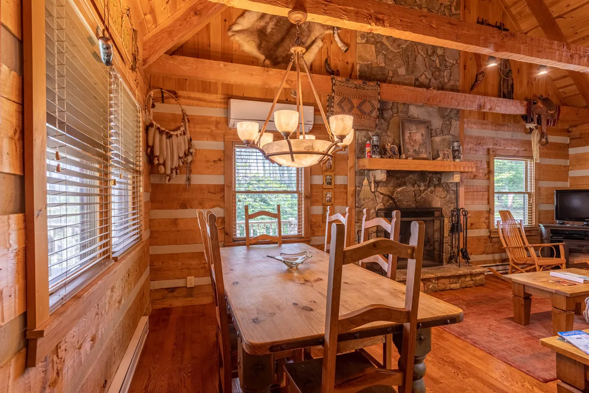 A beautiful dining area highlighted by a wooden table, chandelier, a striking stone fireplace, wooden beams, and stone walls. The setting is intimate yet spacious, perfect for shared meals and storytelling.
