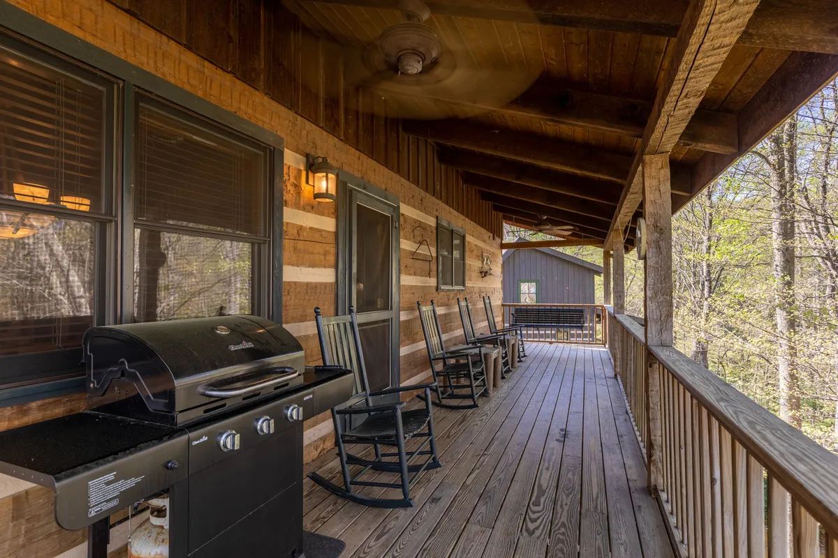 This exterior shot displays a welcoming wooden deck equipped with a grill for barbecuing, rocking chairs for lounging, and sturdy railing that frames a view of the outdoors. The atmosphere is casual and sociable, ideal for gathering with friends or family.